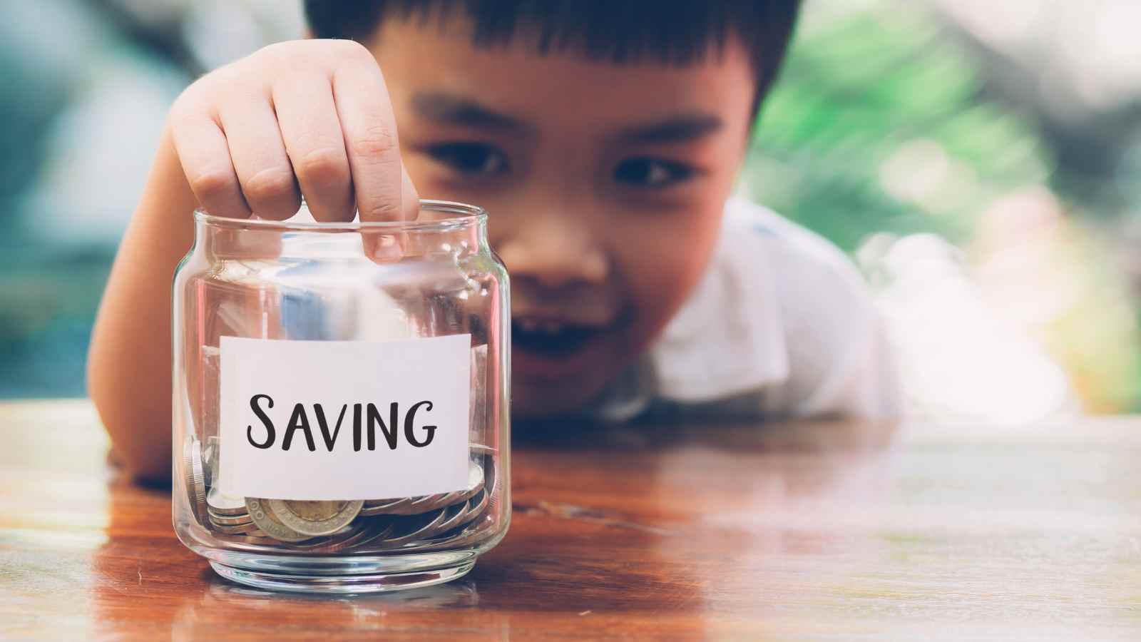 Child putting money into a cup with the label "saving"